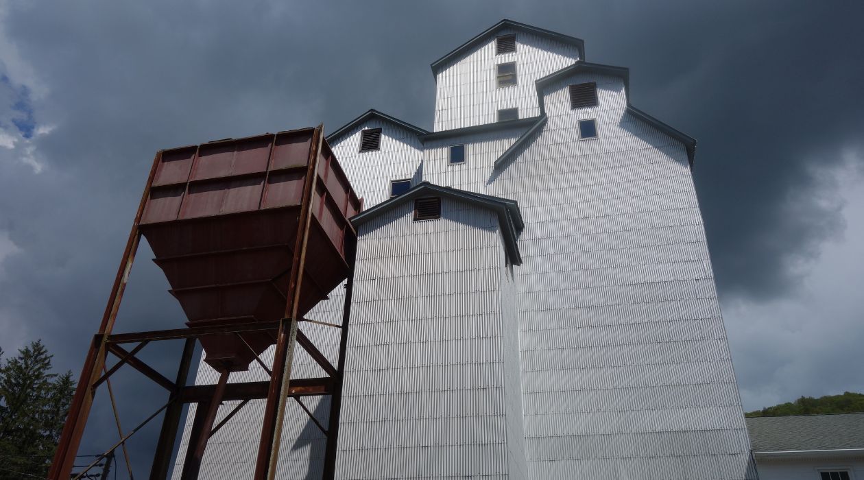 The historic Maxon Mills wooden grain elevator, now the home gallery for the Wassaic Project, towers overhead, its white exterior in sharp contrast against a dark, threatening sky. 